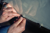 Hands snapping black skirting onto a white adhesive stud on an RV lower trim